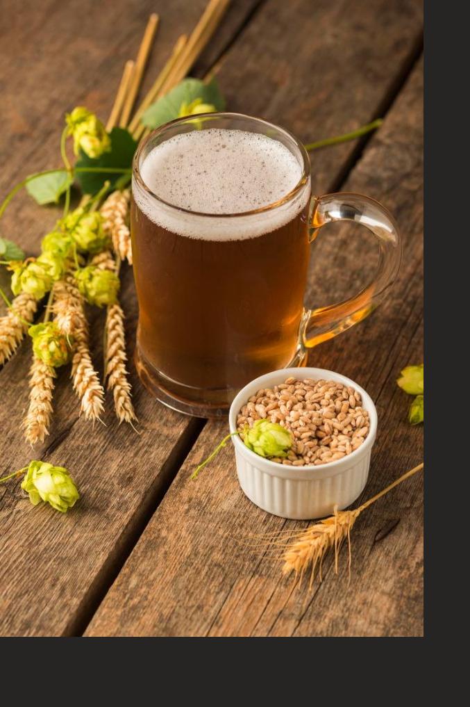 Caneca de cerveja sobre mesa de madeira com cevada e lúpulo